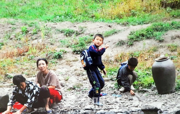 압록강 인근 북한의 일상을 담은 사진 속에서 빨래하는 엄마 옆에서 놀고 있는 아이들 모습.